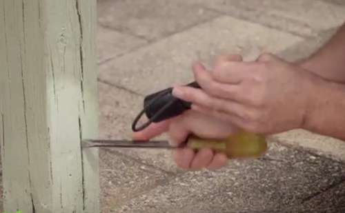 Checking for termites in a wooden pillar with a screwdriver.